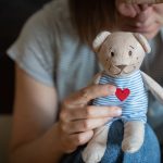 Person holding a stuffed toy dog with a heart on its chest, appearing contemplative.